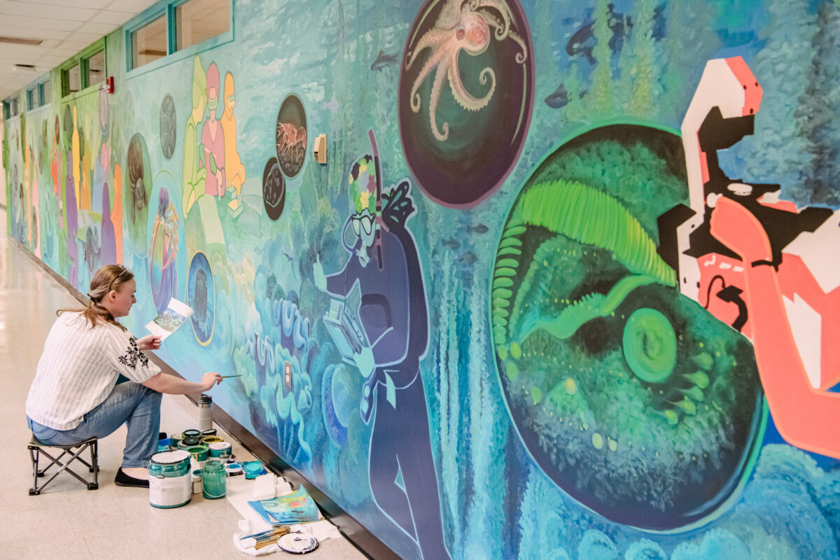 a woman works on repairing a colorful mural representing different biology motifs