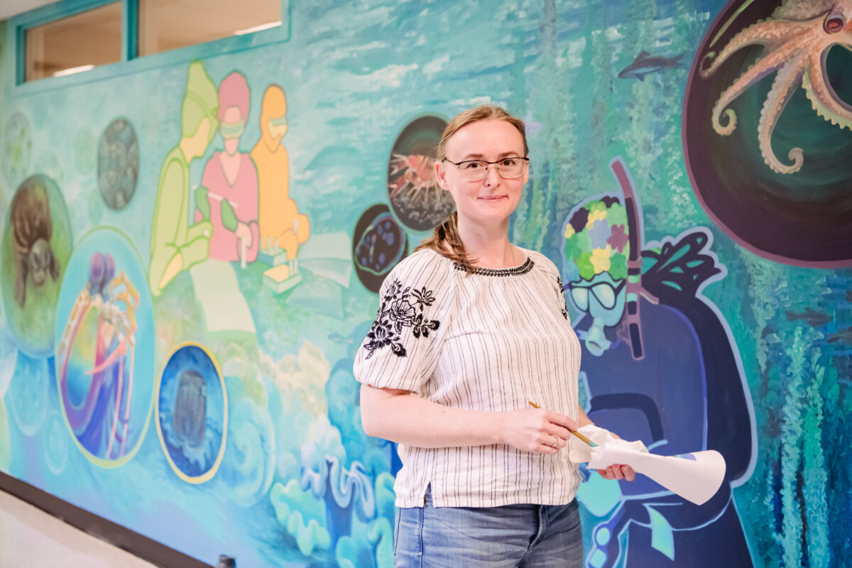 a woman stands in front of a colorful mural representing different biology motifs