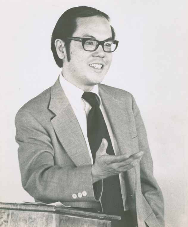 black and white portrait of Calvin B.T. Lee wearing a suit and tie and holding out his hand