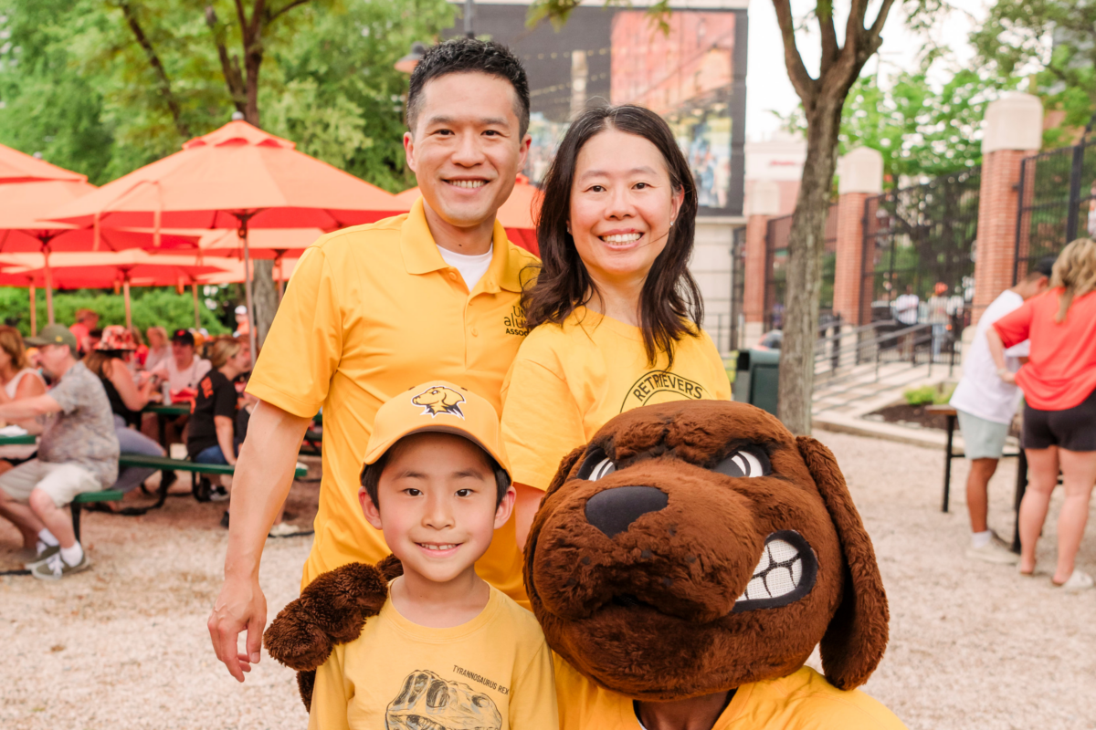 Kevin Yang ’07, computer science and financial economics, and Katelyn Niu ’05, biochemistry, with their son and True Grit at UMBC Night at Camden Yards.