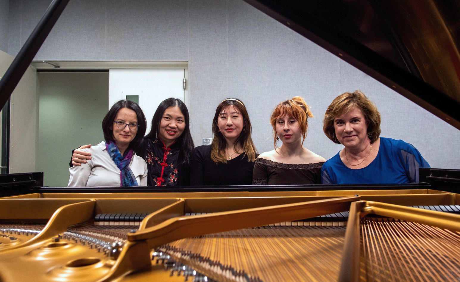 Five women pose behind the strings of a grand piano