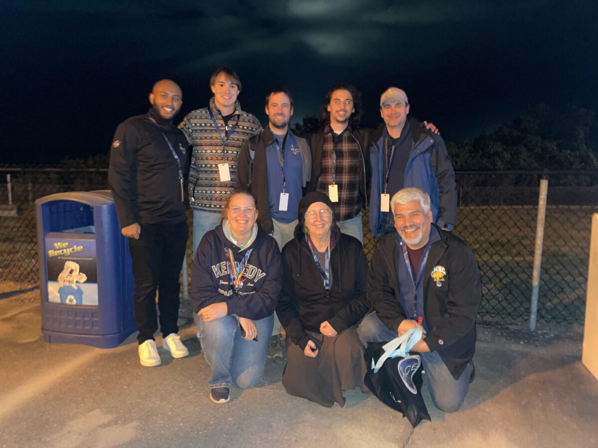 outdoor group photo of eight people, dark night sky in background