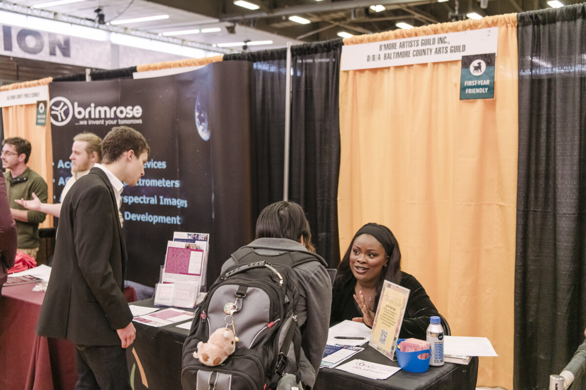 A person sits at a table speaking with students at a UMBC career fair.