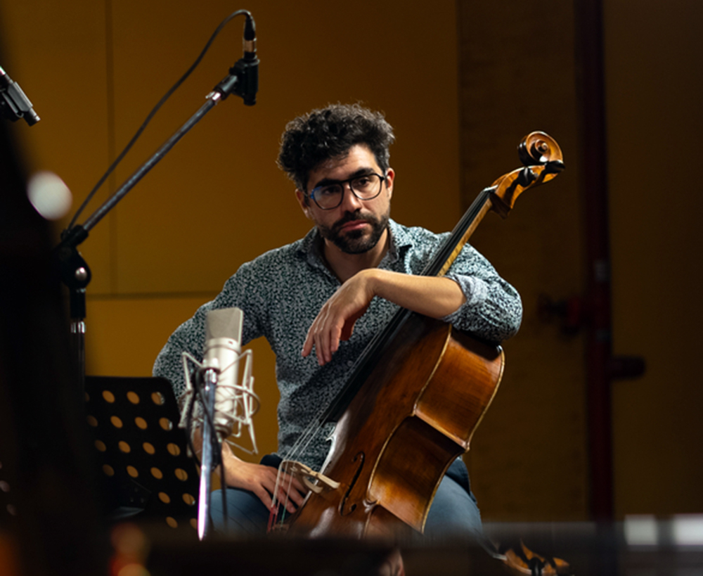 A man with dark hair and glasses poses with a cello