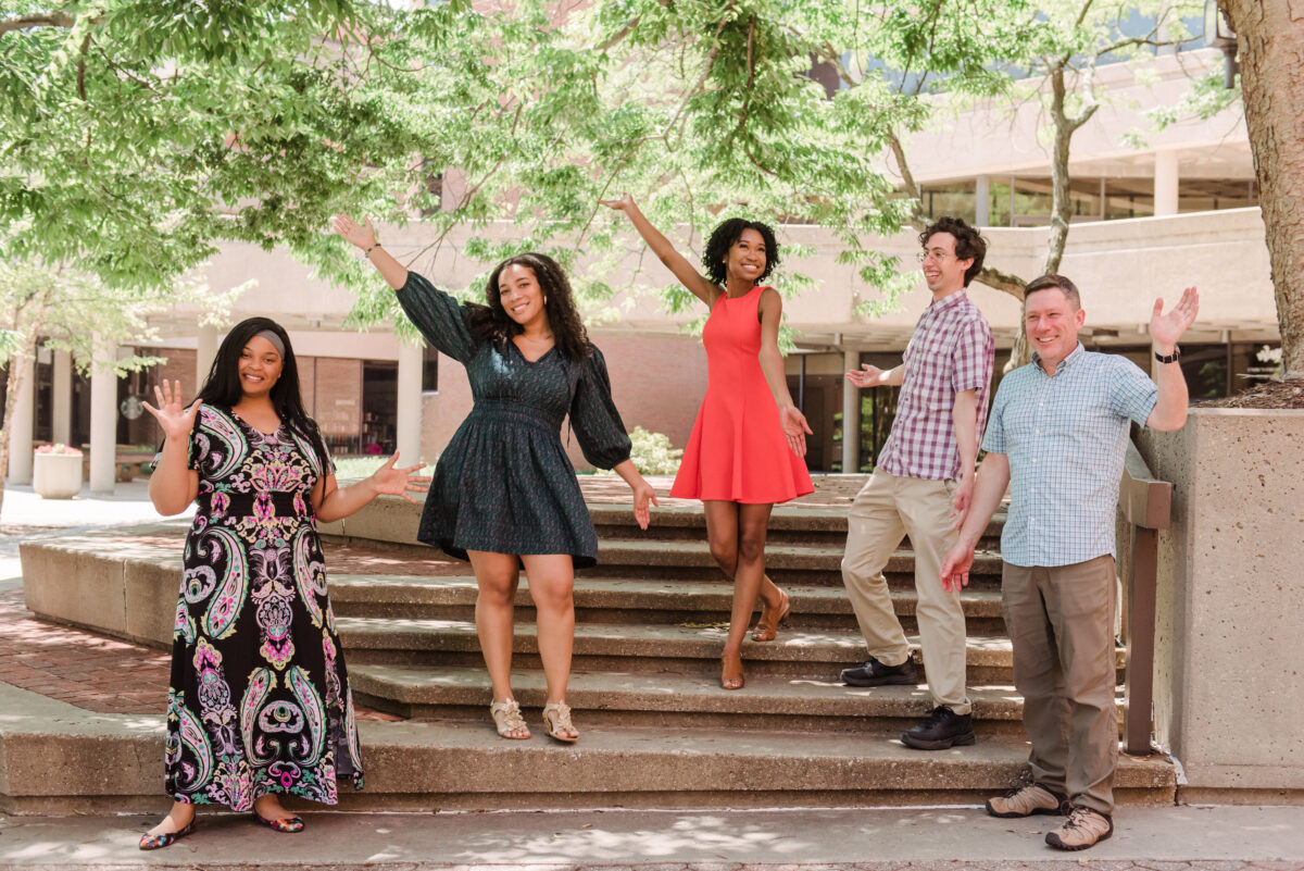 Five Fulbright college students stand outside on concrete steps with their arms outstretched