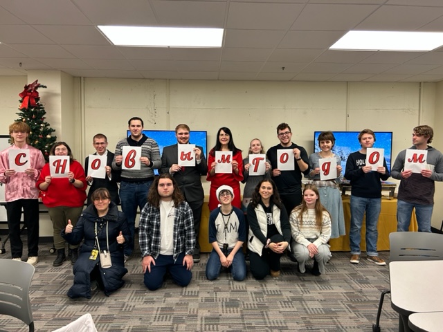 Students learning Russian pose for a photo with their professor, holding up different Russian letters to spell out the phrase "Happy New Year!" in the language.