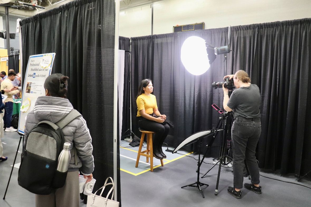 A student sits on a stool while a photographer takes their headshot at the UMBC RAC