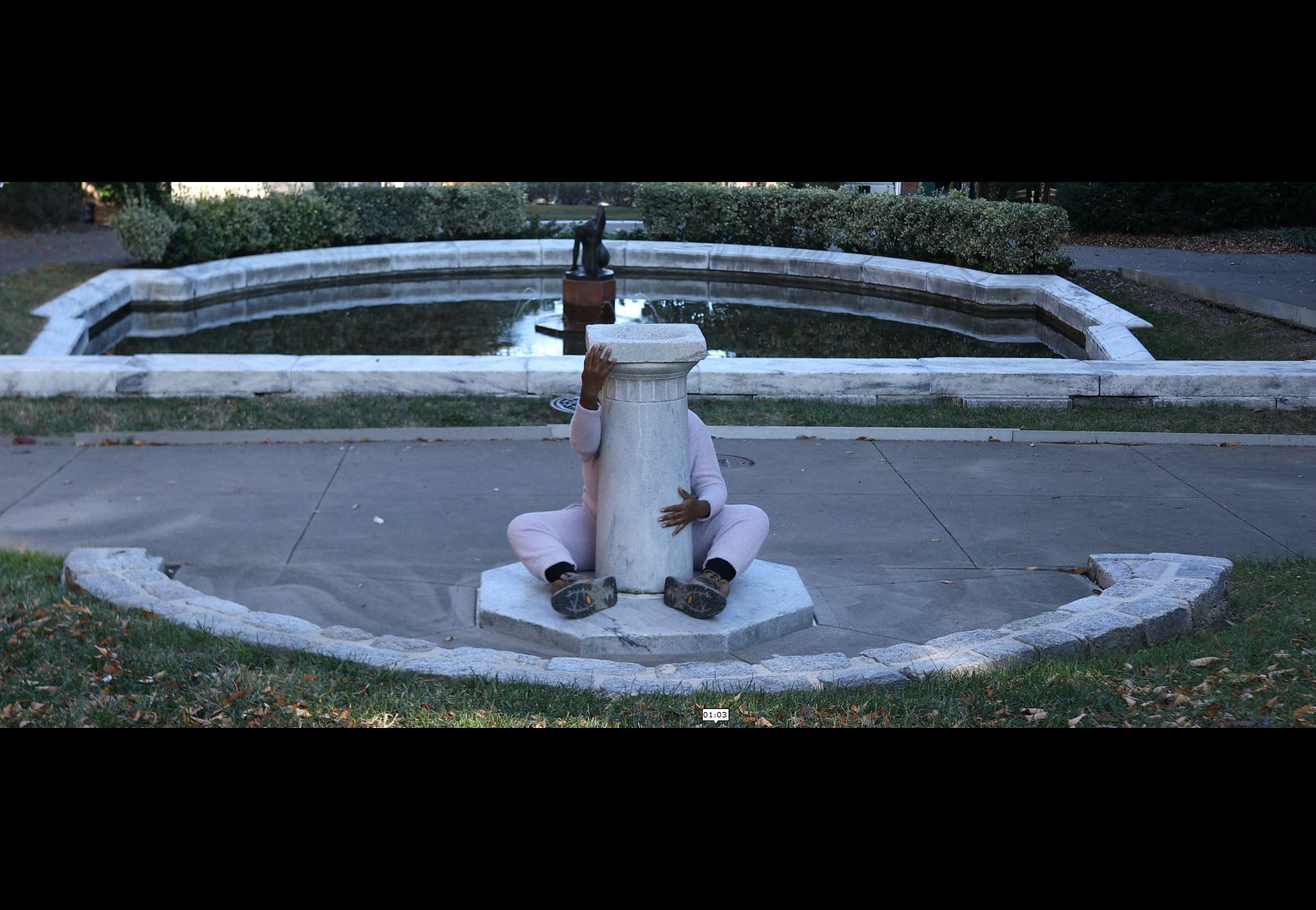 A man wraps himself around a pedestal against the background of a public fountain
