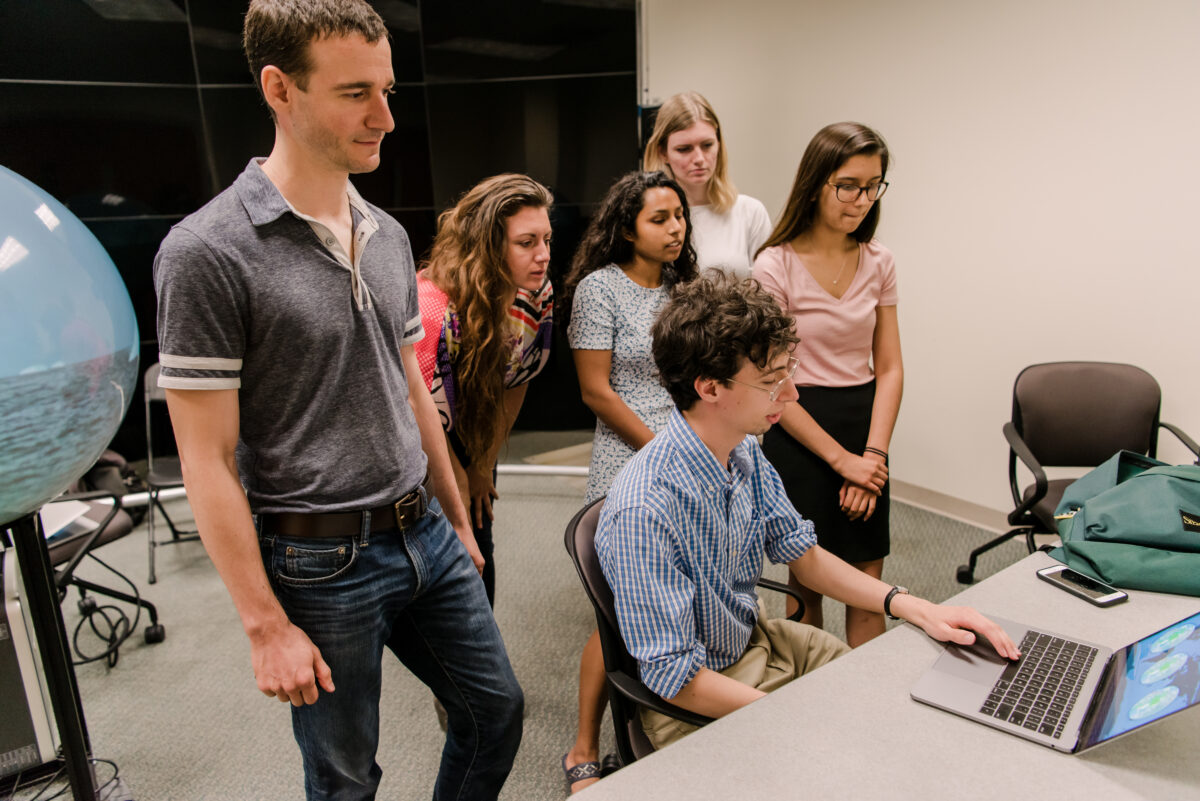 A group of CoLab college students stand around a computer CoLab