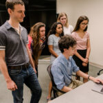 A group of CoLab college students stand around a computer CoLab