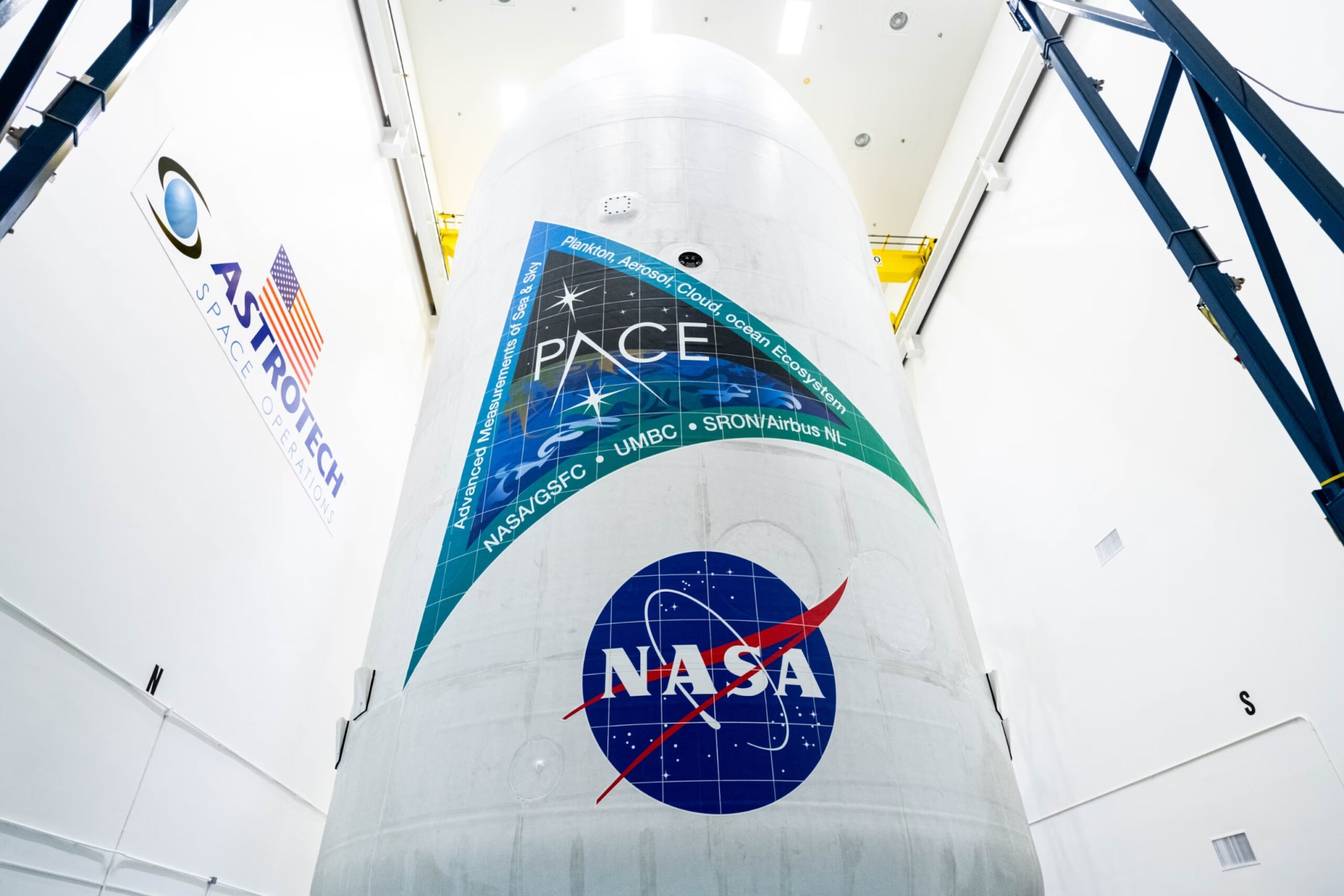 large vertical white cylinder inside a large white room, labeled with "PACE," "NASA," "UMBC" and "SRON/Airbus NL"