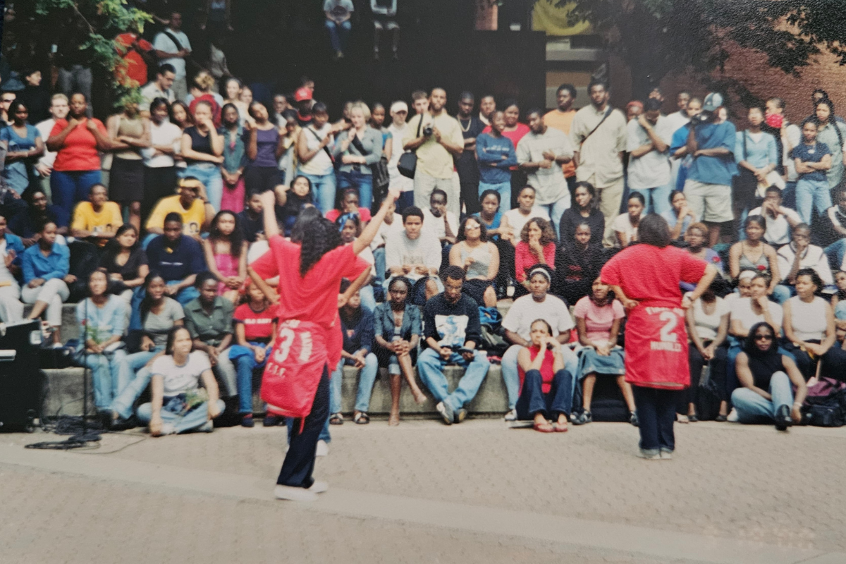 Two sorority sisters dressed in red stand in front of a crowd of students.