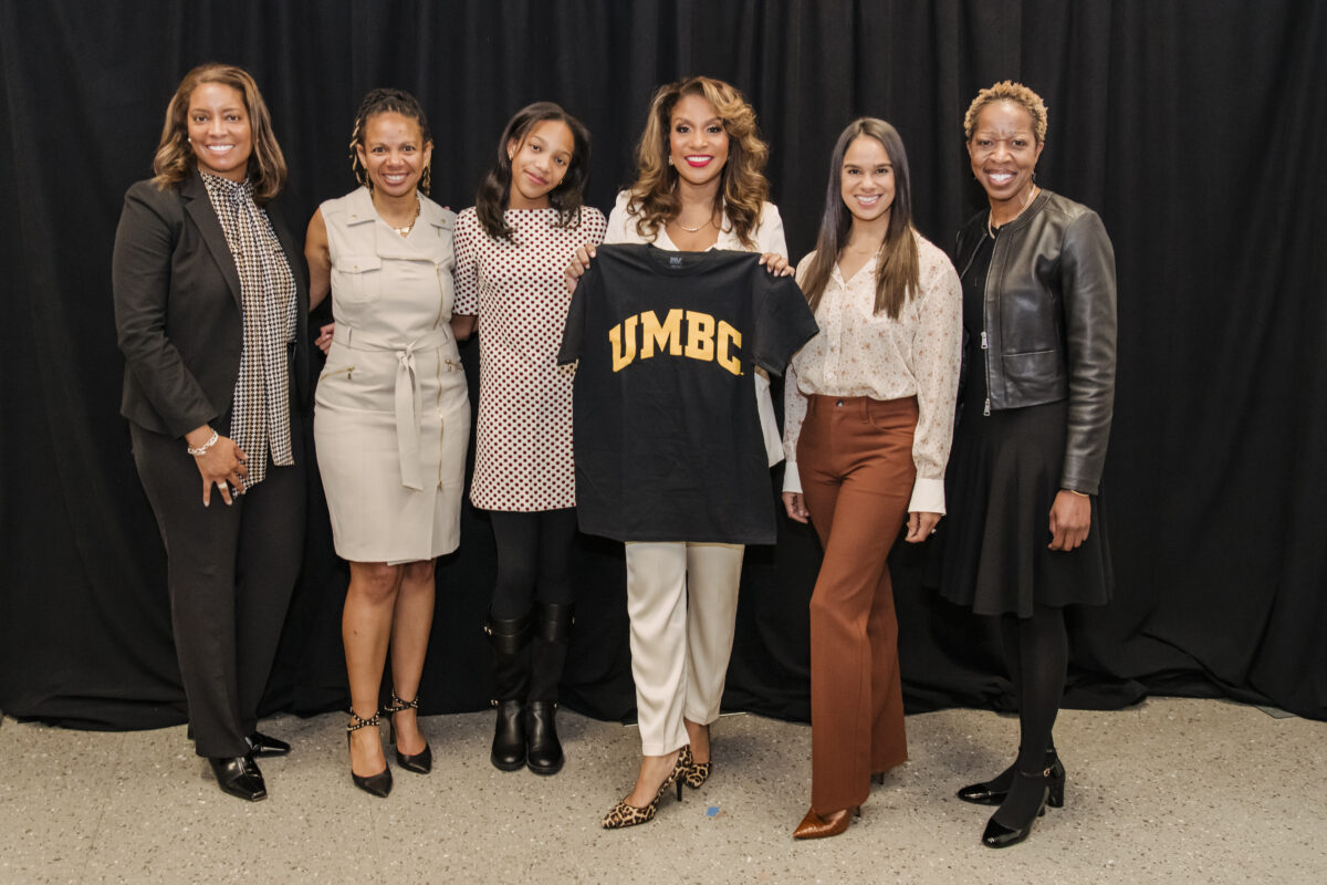 a group of women pose together and one is holding up a t-shirt that says UMBC