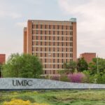 Tall brick building with UMBC sign in foreground. Spring foliage.