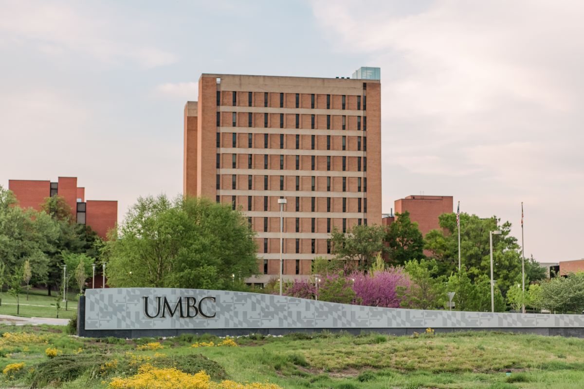 Tall brick building with UMBC sign in foreground. Spring foliage.
