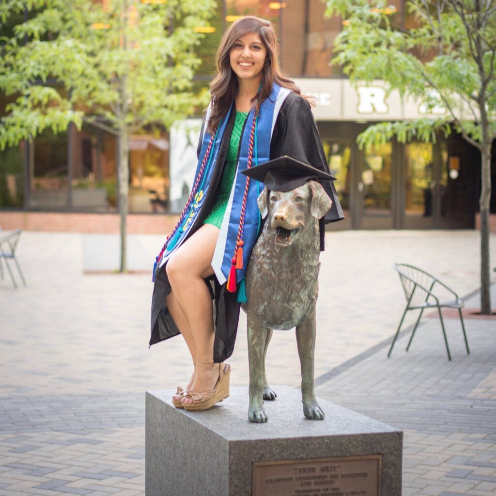 Poulomi Banerjee '16, M.P.P. '21 sitting on the True Grit statue while wearing her graduation gown.