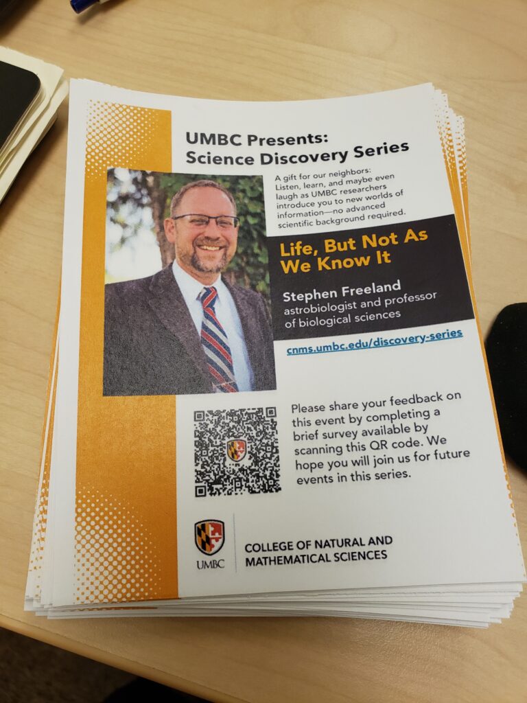 stack of quartercards on a table with headshot of Freeland, short description of the event and talk, and a QR code to the event evaluation form.