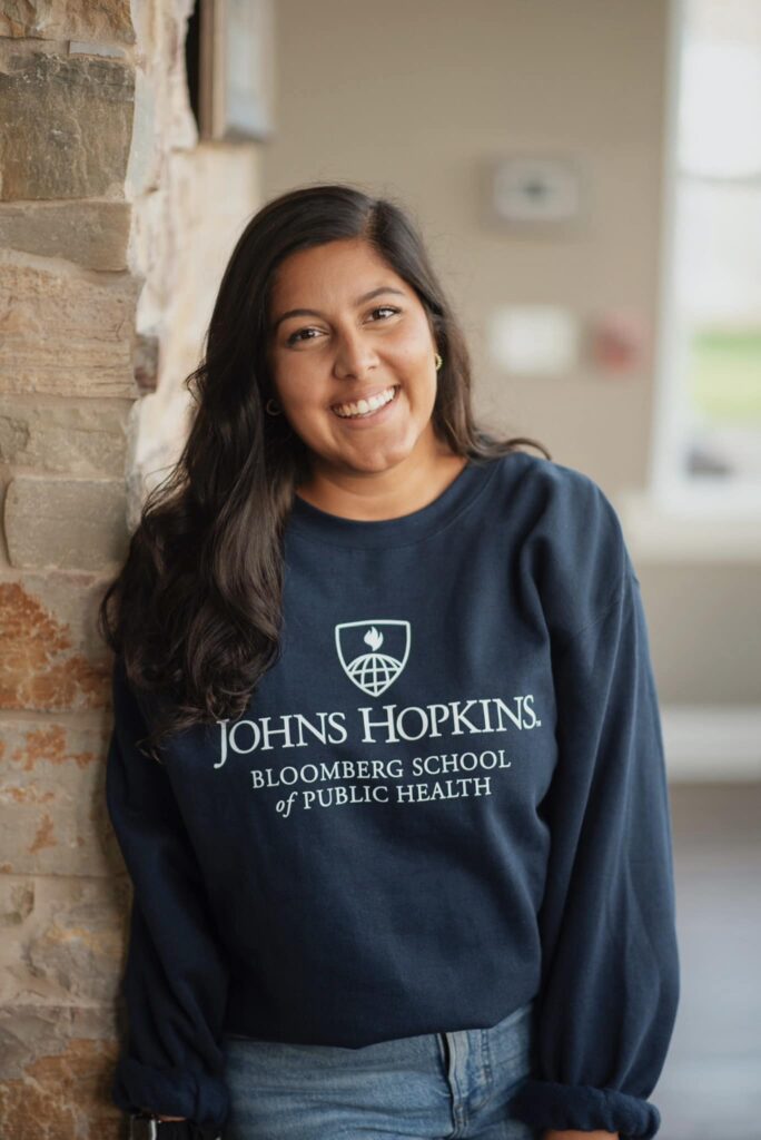 Poulomi Banerjee smiling at the camera wearing a Johns Hopkins Bloomberg School of Public Health sweatshirt.