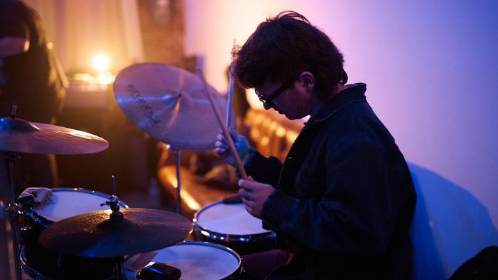Man sitting behind drum kit playing.