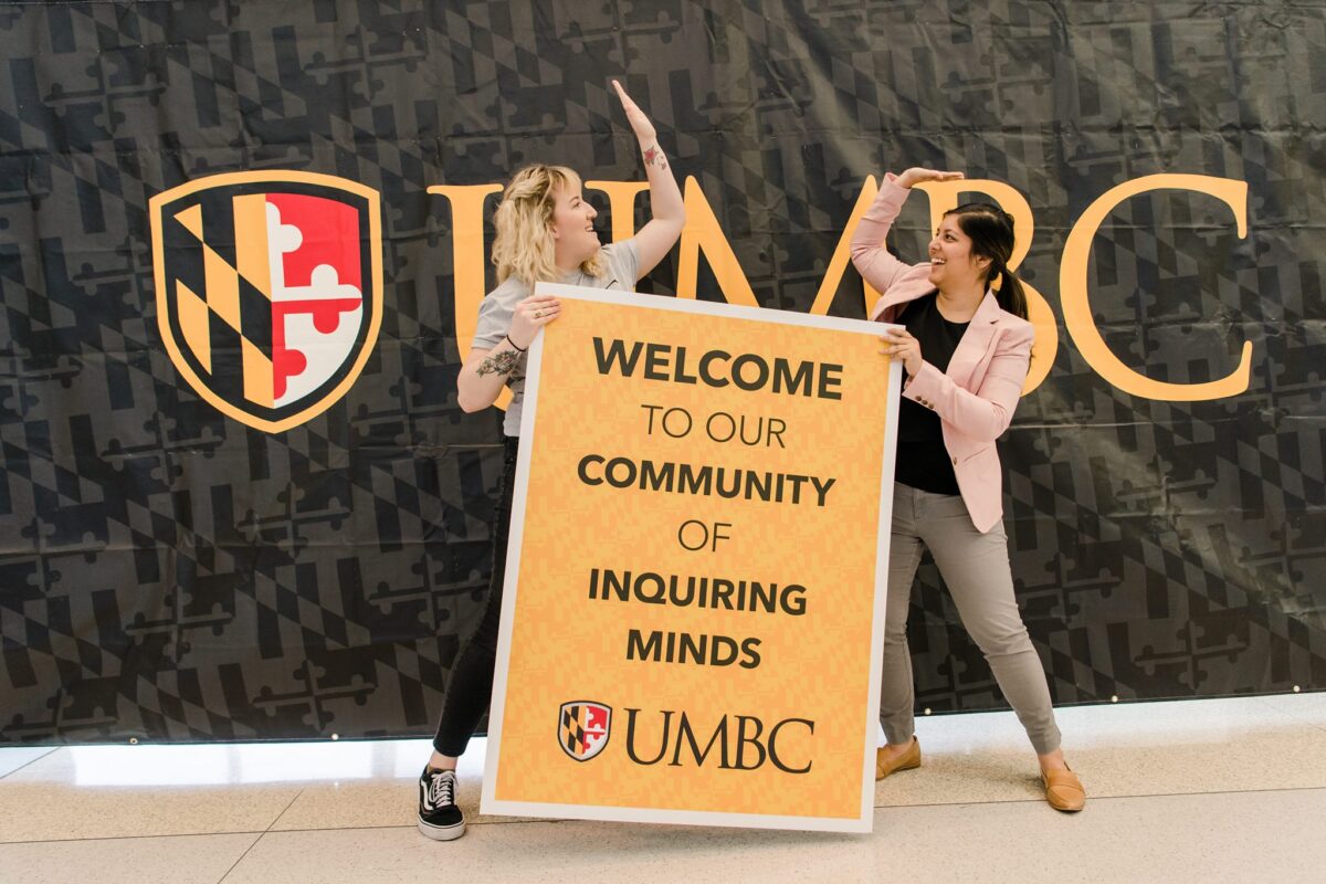 Poulomi Banerjee '16, M.P.P. '21 and Emma Hagen '14 high five while holding a sign that reads Welcome to Our Community of Inquiring Minds