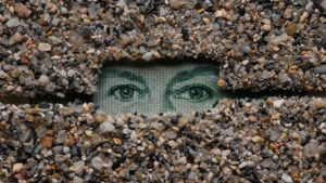 In a work of art, two eyes gaze out from a rectangular enclosure surrounded by small stones.