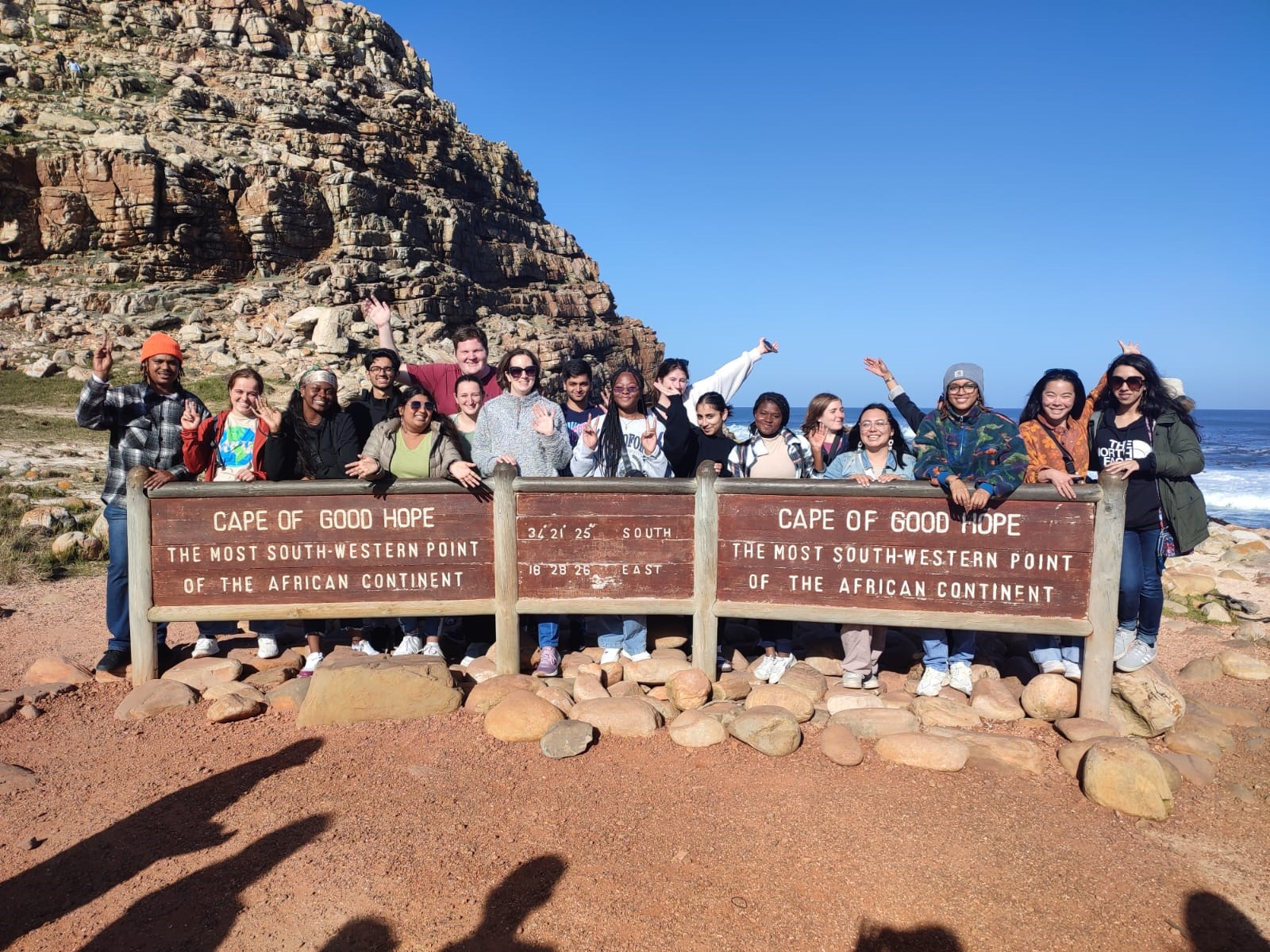 A group of students standing behind a wood sign with the words South Africa written in white on an education abroad trip