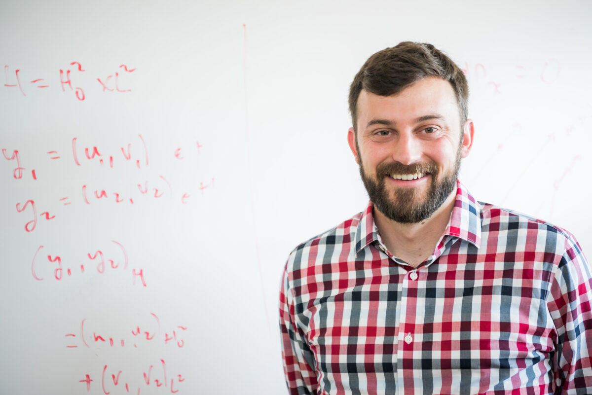 portrait of Justin Webster in front of a whiteboard with equations