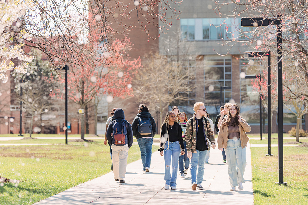 A diverse group of students walk outside together on a sunny Spring day.