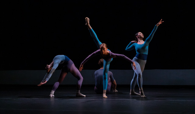 Against a dark background, four dancers perform on stage