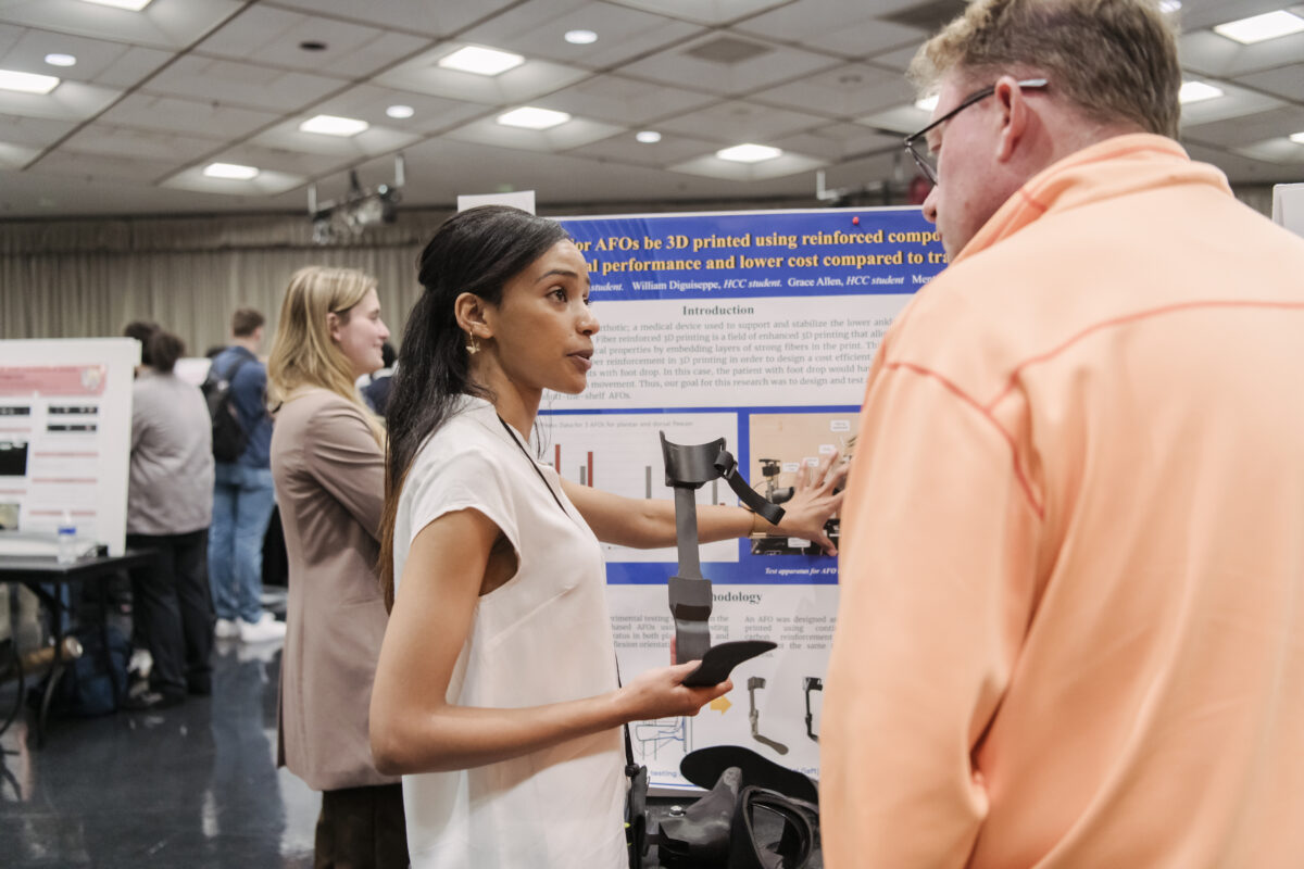 Student holding object that is a part of her research. Student is talking to a visitor of UMBC's Undergraduate Research Day.