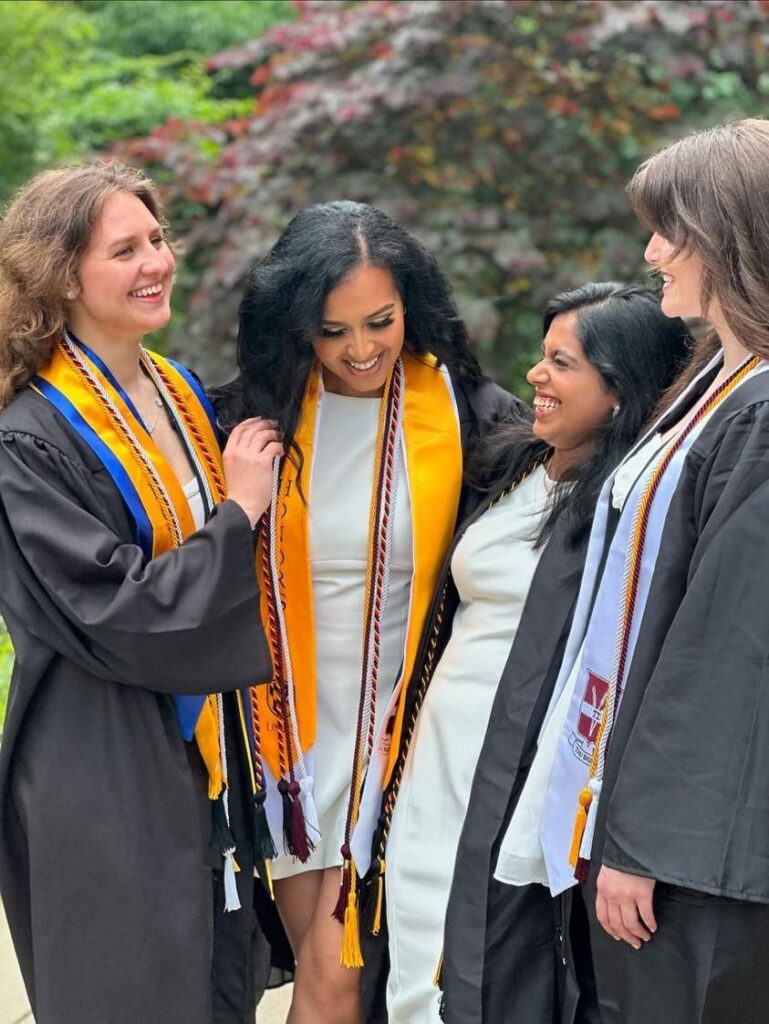 four women from UMBC's translational life sciences program in graduation robes pose together outside