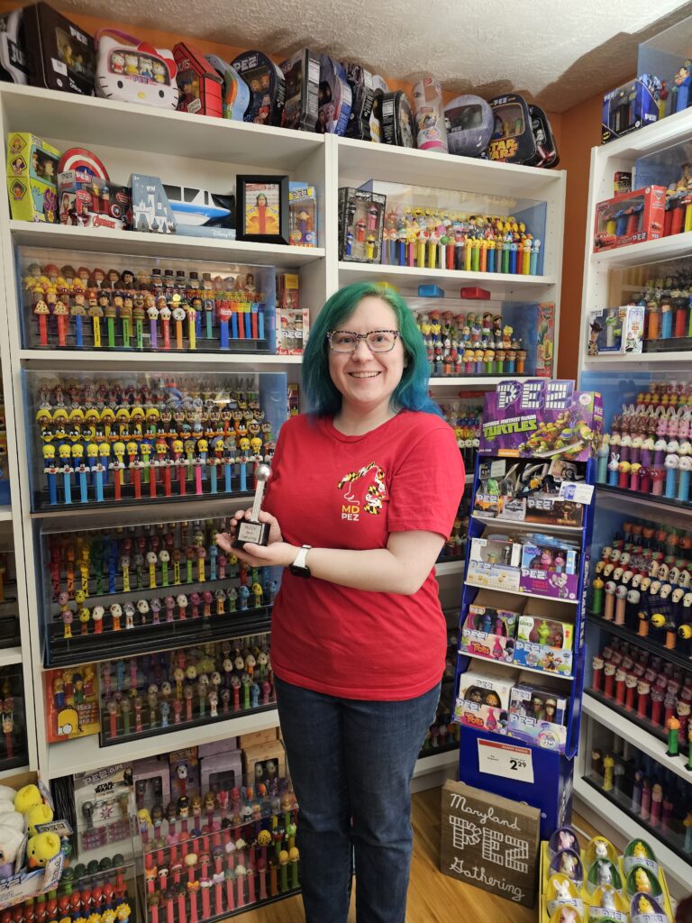a woman with bright green hair stands in front of shelves of thousands of Pez dispensers