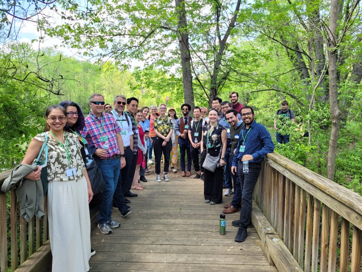 group photo of about 25 people on a wooden footbridge, green trees in the background