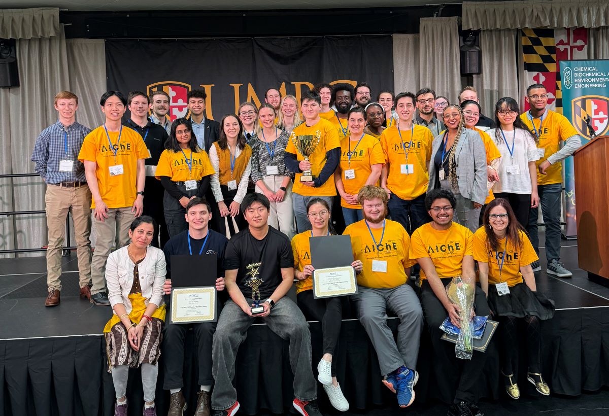 Large group of people, many wearing yellow AIChE shirts, gather on stage and pose for the camera.