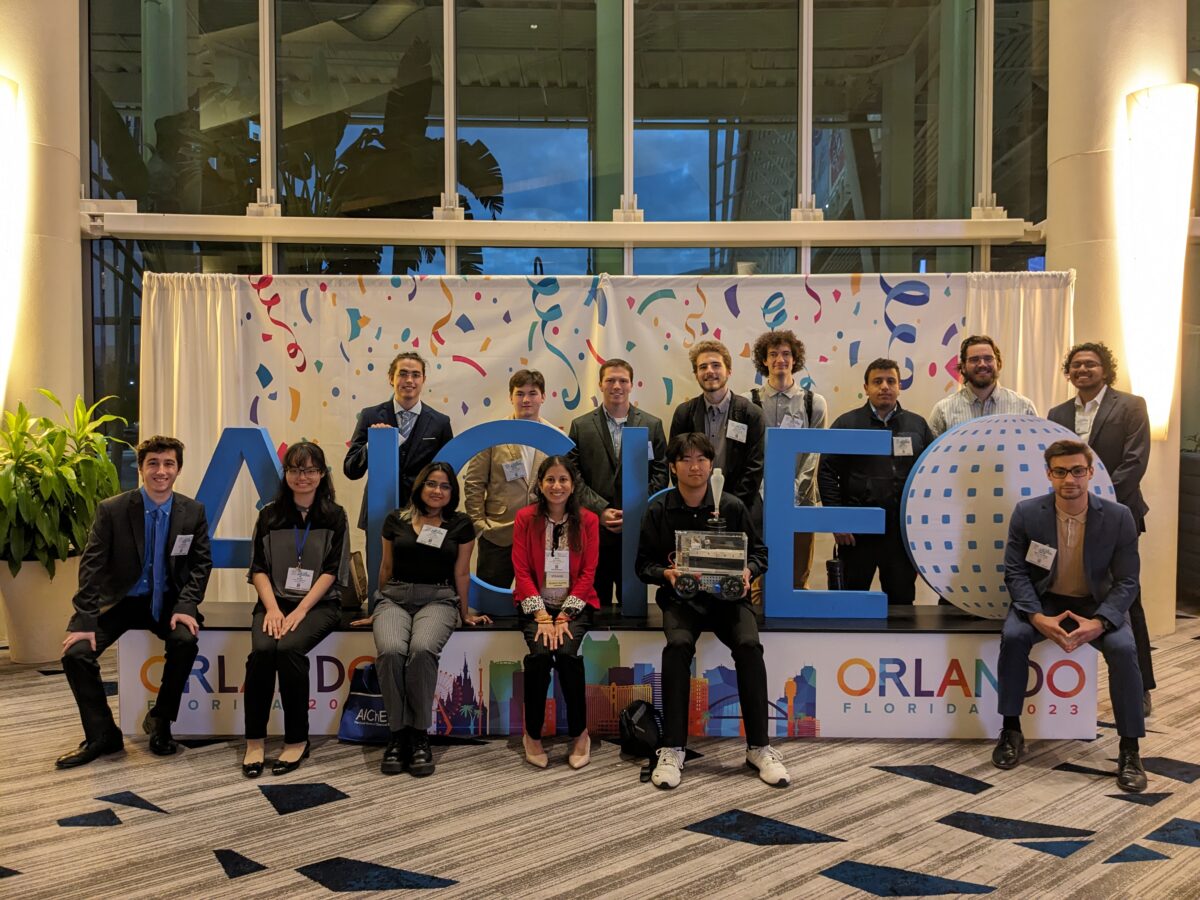 14 people sit or stand near a AICHE, Orlando sign