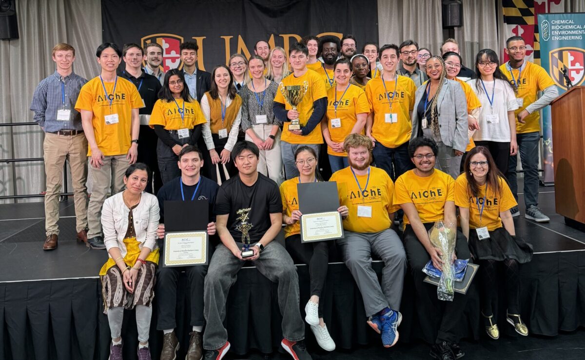 Large group of people, many wearing yellow AIChE shirts, gather on stage and pose for camera.