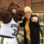 Connie Pierson and the UMBC mascot, True Grit, standing arm in arm and pointing at the camera.