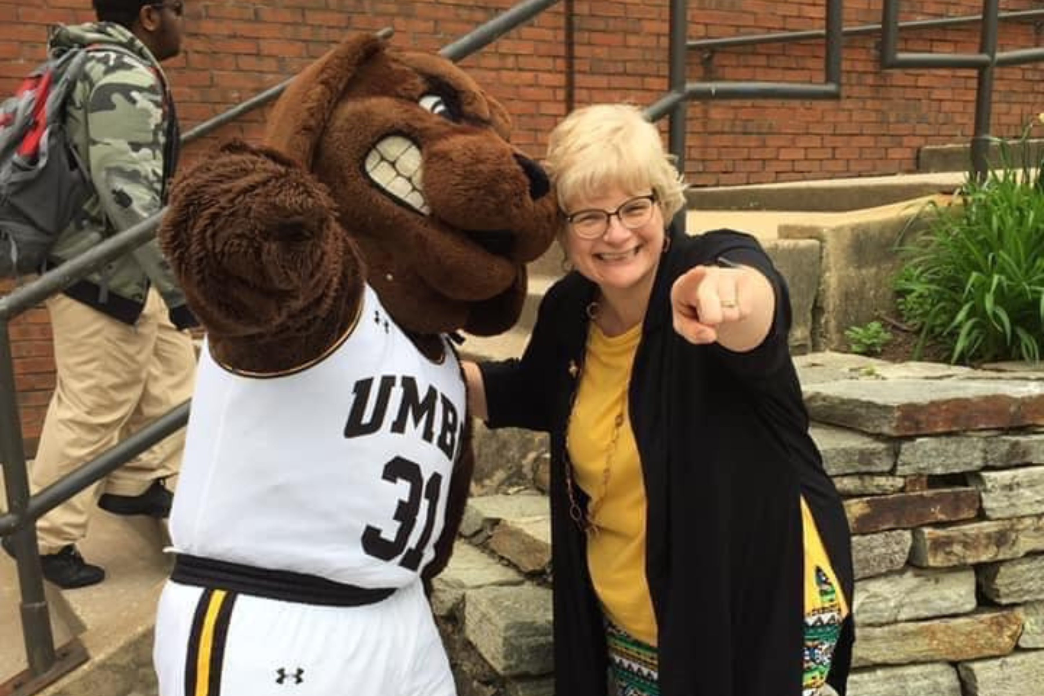 Connie Pierson and the UMBC mascot, True Grit, standing arm in arm and pointing at the camera.