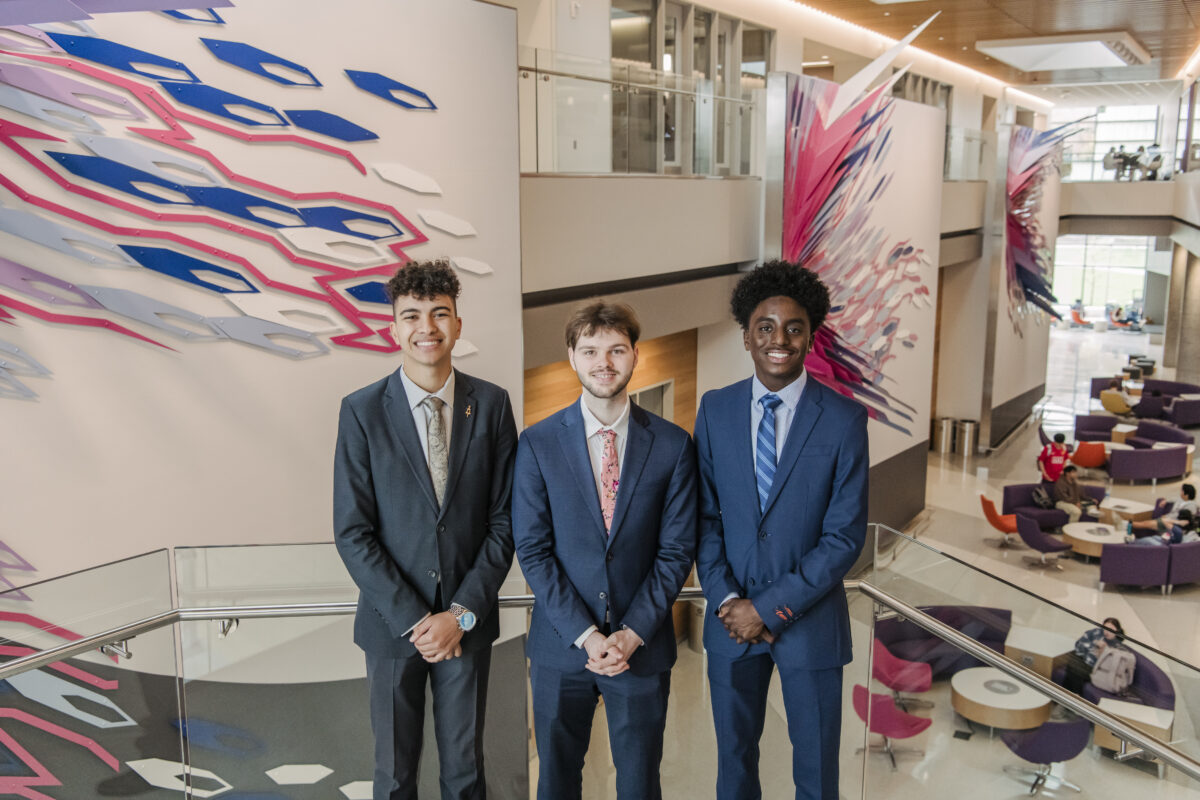 Three college students who are wearing suits smiling at the camera on UMBC's campus. Students are 2024 Goldwater Scholarship recipients.