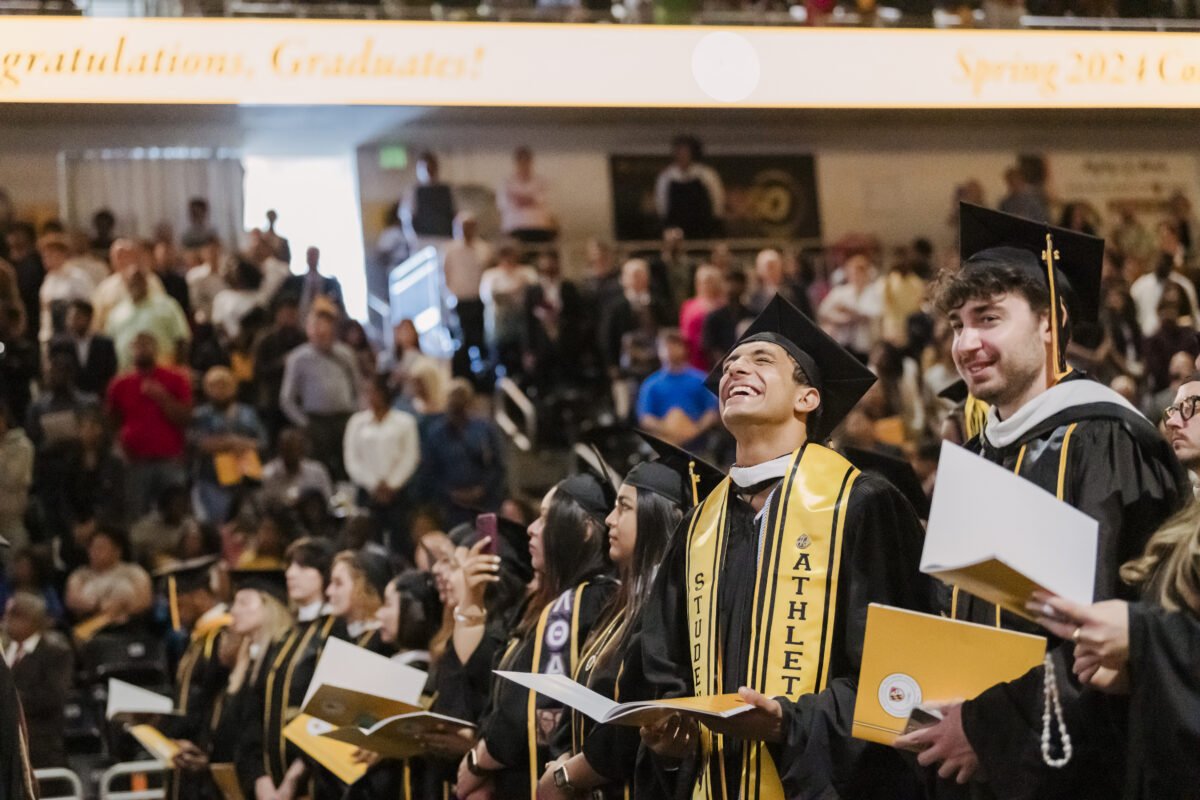 UMBC Class of 2024 graduate who has a student athlete graduation sash on looking upward and smiling with joy. 