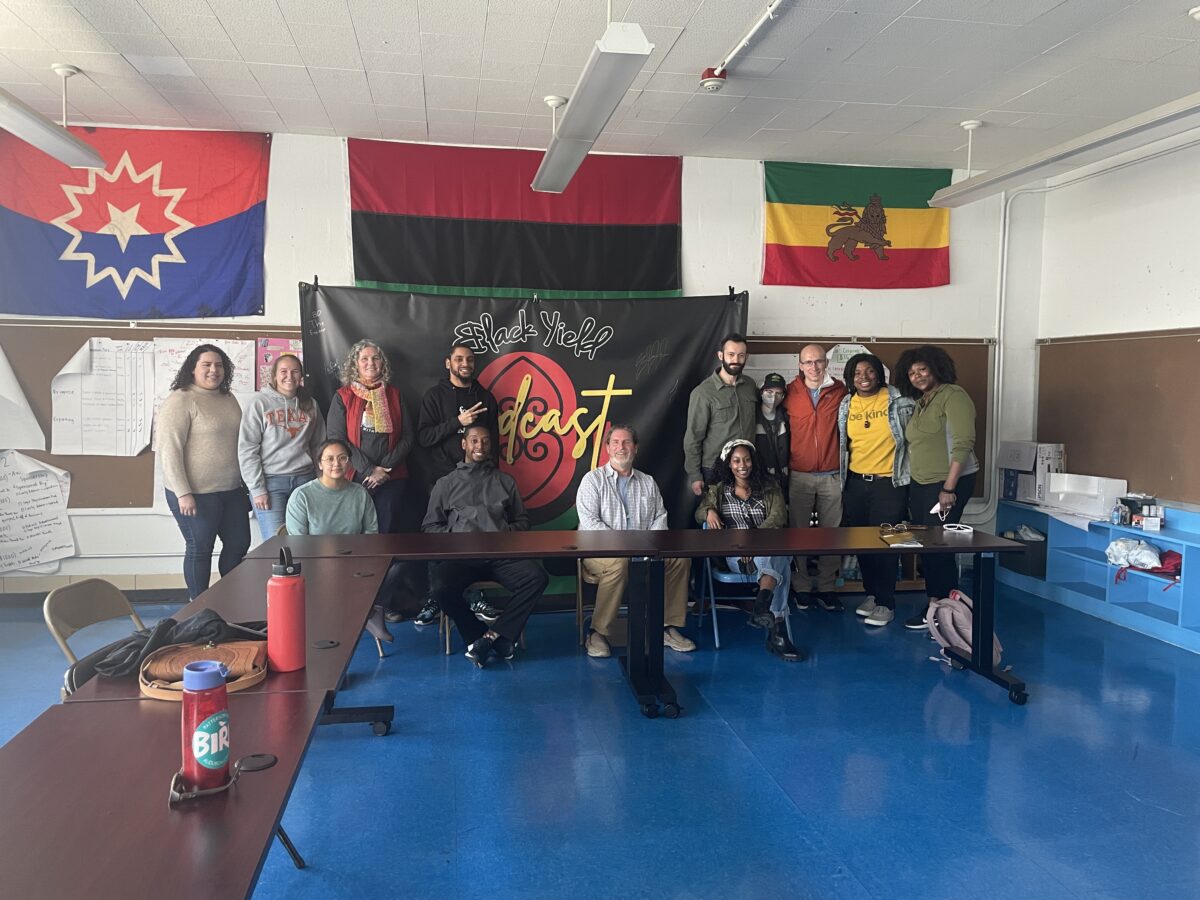 A group of UMBC Peaceworker Fellows in front of flags smiling 
