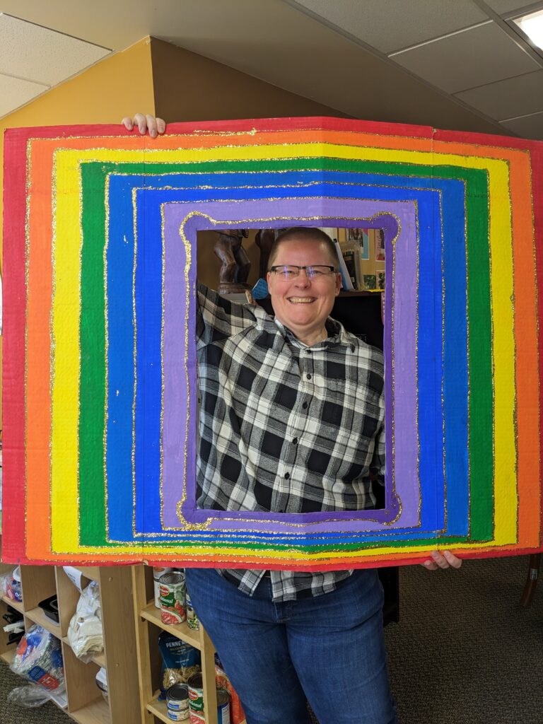 A person holds a large rainbow social media picture frame