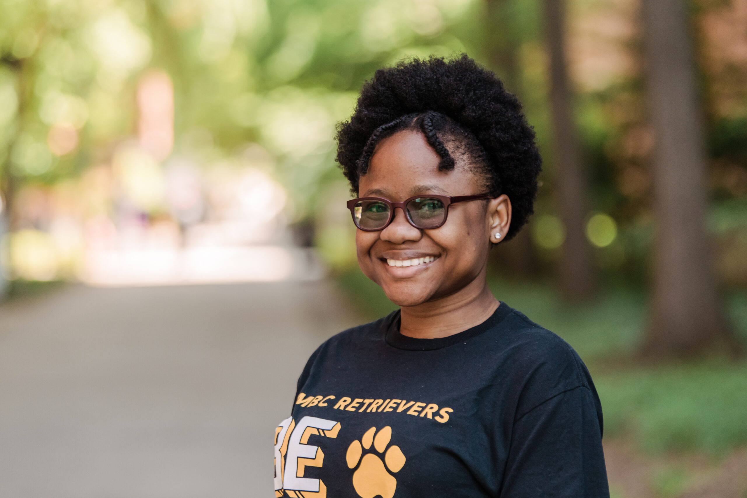 A college student wearing a black and gold t-shirt standing on a walk way in a college campus
