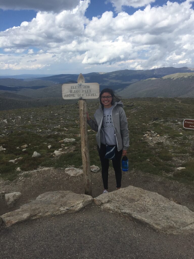a female student stands next to a sign in the mountains