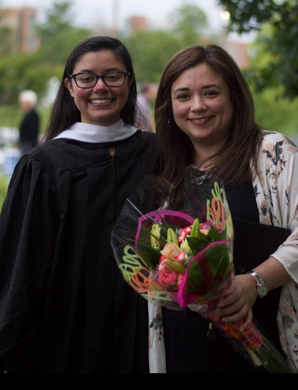 Two women pose outside, one of them wearing graduation regalia