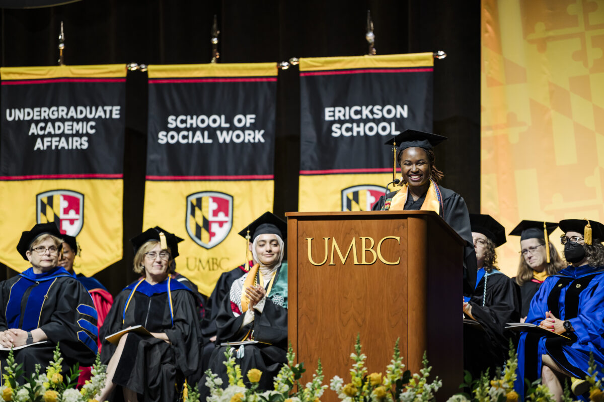 Valedictorian for the College of Arts, Humanities, and Social Sciences; School of Social Work; and Erickson School of Aging Studies morning ceremony, Nyla Howell, speaks at Commencement. Nyla is standing behind a podium while on stage. 