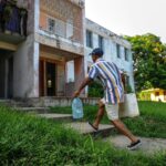 A person in the Caribbean carries large plastic jugs of water into an old apartment building