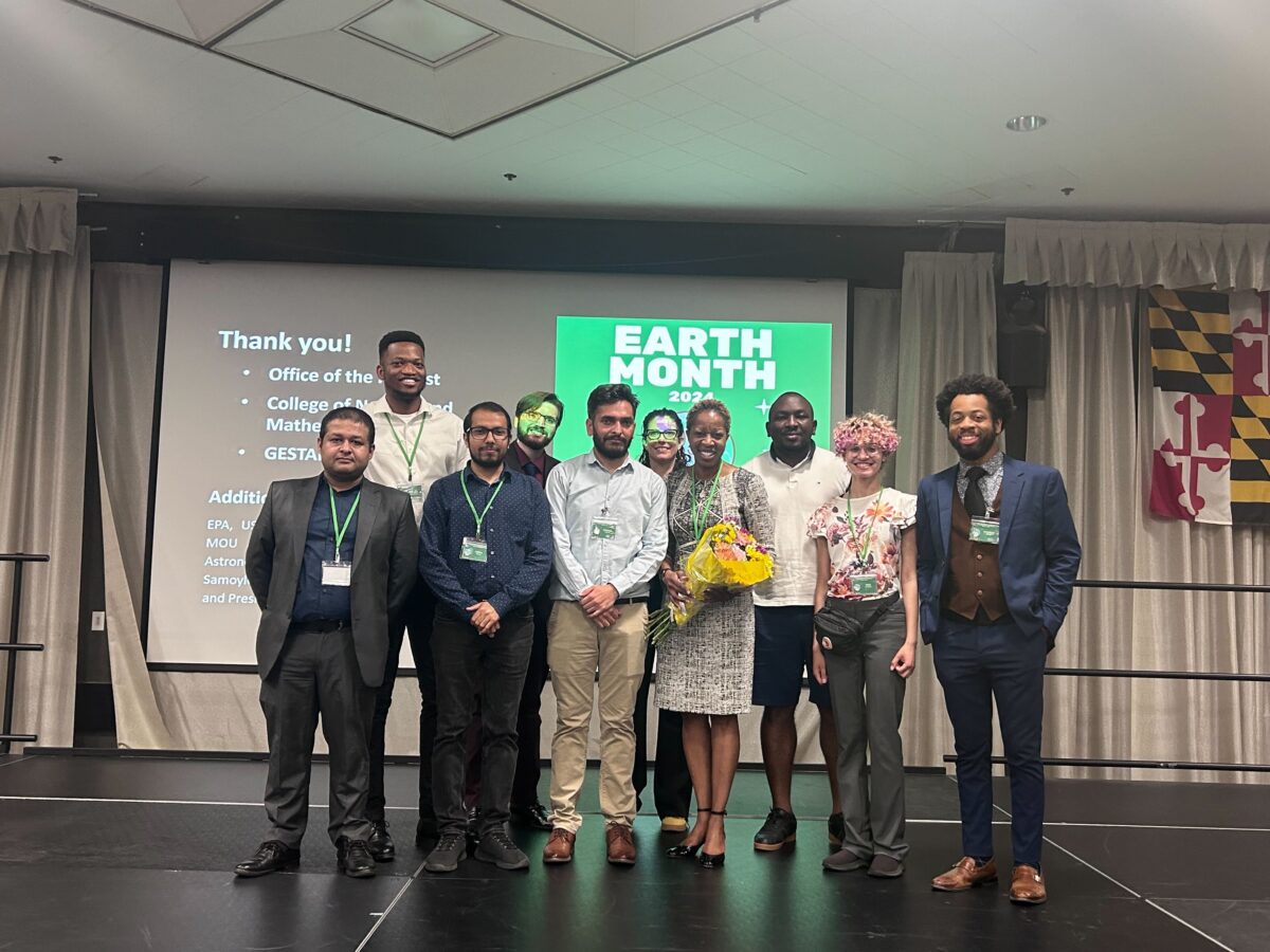 group photo of 10 people - the Earth Day Symposium planning committee - on a stage in front of a screen. The top portion of the screen is visible and reads "Earth Month."