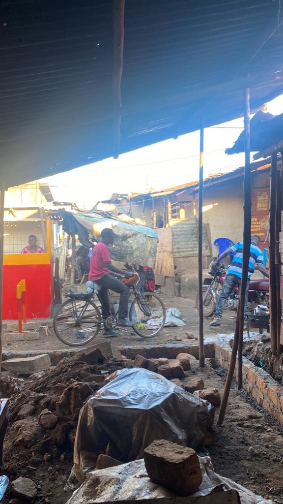 Cyclists bike through a neighborhood of small shacks 