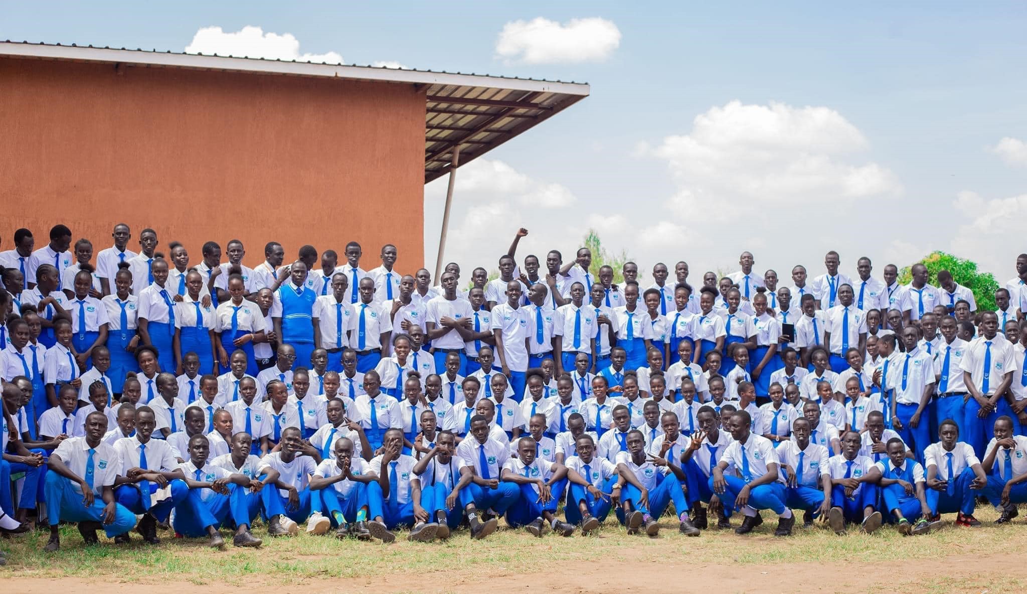 A large group of young of high school students from the Promised Land Primary and Secondary School in South Sudan wearing blue and white uniforms gather to take a photo.